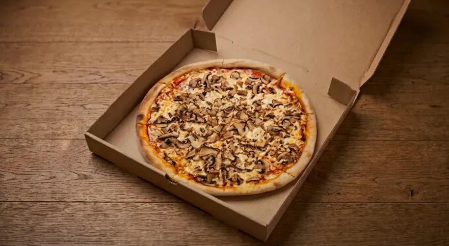 Pizza s gljivama i sirom u kartonskoj kutiji na drvenom stolu